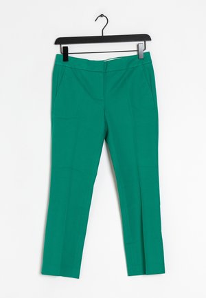 Pantalons taper verts avec une texture lisse, dotés de deux poches latérales et d'une fermeture éclair. Accrochés à un cintre en plastique noir.