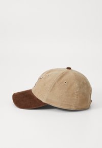 Corduroy cap with a beige body and brown visor. Features raised embroidery and ventilation holes. Classic curved brim design.