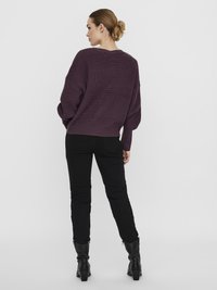 Oversized purple knitted sweater with a v-neck, paired with black slim-fit jeans and textured black heeled boots, viewed from the back.