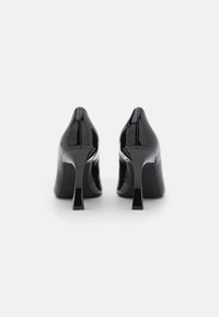 Zapatos de tacón alto de charol negro con punta afilada y un tacón delgado y angular. Textura suave con un acabado pulido.