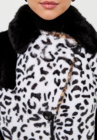 Ceață din blană artificială cu imprimeu de leopard, cu margini negre și o textură moale; dispune de un guler și nasturi negri pe partea din față.