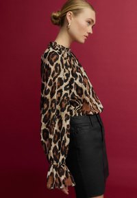 Blůza s leopardím potiskem, s nafouklými dlouhými rukávy a volánkovým límcem, zkombinovaná s černou sukní. Hladká textilie. Odvážný zvířecí vzor.