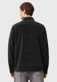 Black corduroy jacket with a collar, featuring a textured fabric and buttoned cuffs. Back view shows simplicity in design and structure.