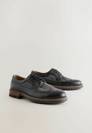 Black leather dress shoes with a textured herringbone pattern, brogue detailing, and a sturdy brown wooden heel.