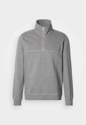 Szara bluza zapinana na zamek z wysokim kołnierzem, o miękkiej teksturze i kontrastowym przeszyciu. Posiada szew na klatce piersiowej oraz logo na rękawie.