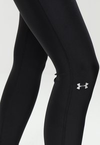 Czarne legginsy sportowe wykonane z elastycznego materiału, o gładkiej fakturze, slim fit oraz srebrnym logo na dolnej części nogawki.