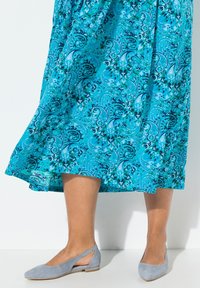 Niebieska sukienka w wzór paisley z zwiewnego materiału, zestawiona z jasnoniebieskimi zamszowymi balerinami z odkrytą piętą i lekko podwyższonym obcasem.