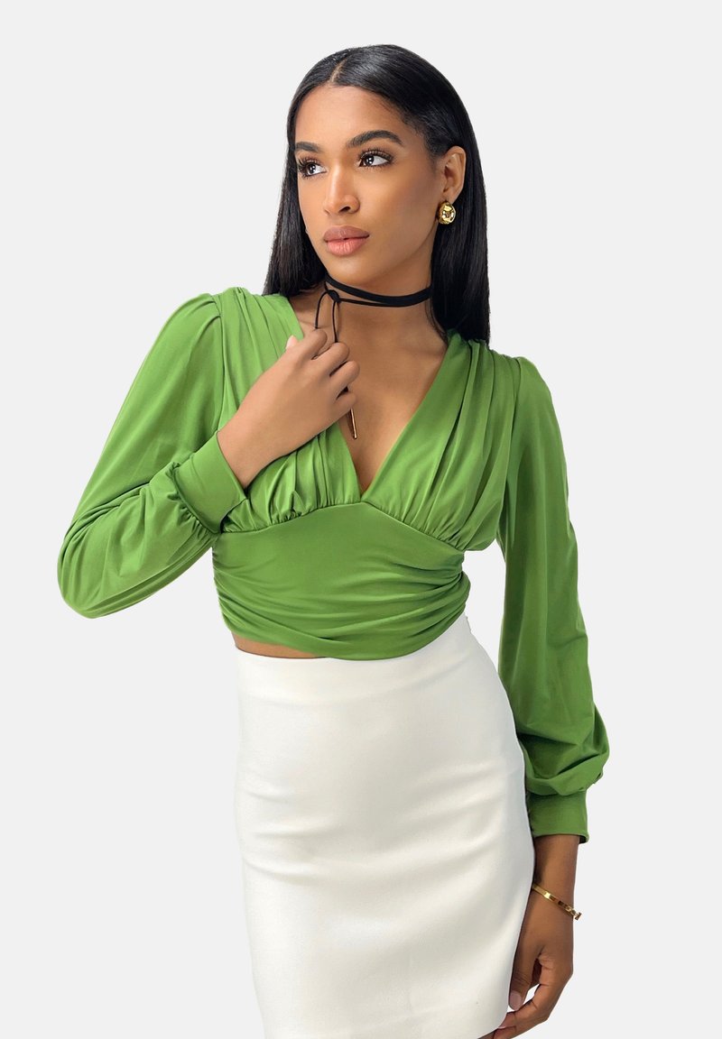 Top cropped verde a maniche lunghe con scollatura a V e dettagli arricciati, abbinato a una gonna bianca aderente. Tessuto testurizzato e finitura liscia.
