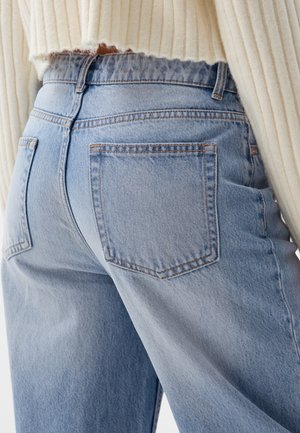 Jean en denim bleu clair à taille haute, avec deux poches arrière et des détails de couture discrets. Le tissu a une finition lisse et texturée.