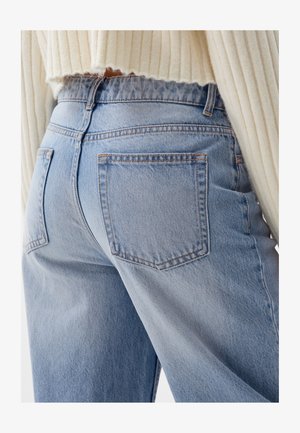 Jeans in denim blu chiaro con vita alta, dotati di due tasche posteriori e dettagli di cucitura sottili. Il tessuto ha una finitura liscia e texturizzata.