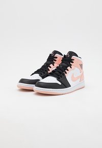 Para czarnych, białych i jasnoróżowych wysokich sneakersów Air Jordan z czarnymi sznurówkami na białym tle.