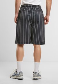 Shorts noirs avec des rayures verticales blanches, une taille élastique et une coupe décontractée, associés à des chaussures de sport grises et bleues et des chaussettes blanches.
