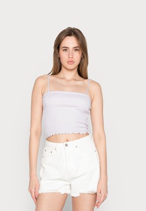 Gehaakte crop top in licht lila met rimpelige randen, gecombineerd met witte high-waisted denim shorts met rafelige zoom en voorkeurszakken.