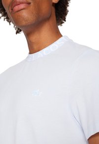 Jasnoniebieska bawełniana koszulka z okrągłym dekoltem, białym kołnierzykiem z logo marki i małym wytłoczonym logo na piersi. Gładka tekstura.