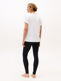 Hvit kortermet skjorte kombinert med svarte leggings. Enkelt design, bomullsmateriale, tettsittende leggings og bare føtter mot en nøytral bakgrunn.