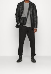 Giacca di pelle nera, maglione grigio a coste, pantaloni neri e stivaletti neri alla caviglia. Una piccola borsa a tracolla nera è indossata in diagonale.