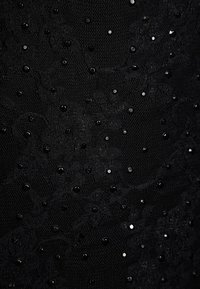 Tela de encaje negro con un intrincado patrón floral, adornada con lentejuelas negras y plateadas para darle textura y detalles visuales.
