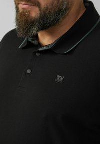 Schwarzes Poloshirt aus weichem Stoff, mit kontrastierendem Kragen, zwei Knöpfen und einem kleinen Logo auf der Brust.