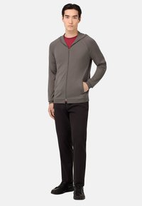 Sivá mikina na zips s prednou kapsou, raglánovými rukávmi a kapucňou. V kombinácii s čiernymi nohavicami a čiernymi teniskami. Jednoduchý a funkčný dizajn.