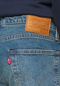Tylny kieszeń dżinsów z denimu z czerwoną metką Levi's oraz brązową skórzaną naszywką Levi Strauss & Co., na której widnieje rozmiar W32 L34.
