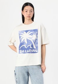Majica od pamuka u boji krem sa kratkim rukavima, s plavim grafičkim dizajnom palmi i sunca, te riječju "BILLABONG" u bijeloj boji.