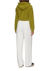 Oliwkowa bluza z kapturem i kieszenią kangurzą, zestawiona z białymi spodniami o szerokich nogawkach. Miękki materiał z elastycznym pasem. Sneakersy z teksturowaną platformą.
