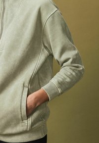 Oliv roheline pullover sviiter kõrge kaelusega, soonikkoes varrukatega, küljetasku ja pehme, tekstuuriga kangas.