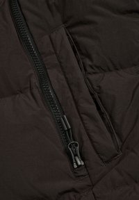 Zwarte pufferjas sectie met een ritszak en een gladde textuur, voorzien van een plastic rits en zwarte hardwareaccenten.