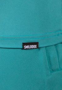 Turkusowy materiał o gładkiej fakturze, z czarną metką z napisem "SMILODOX" na górze i detalem szwu poniżej.