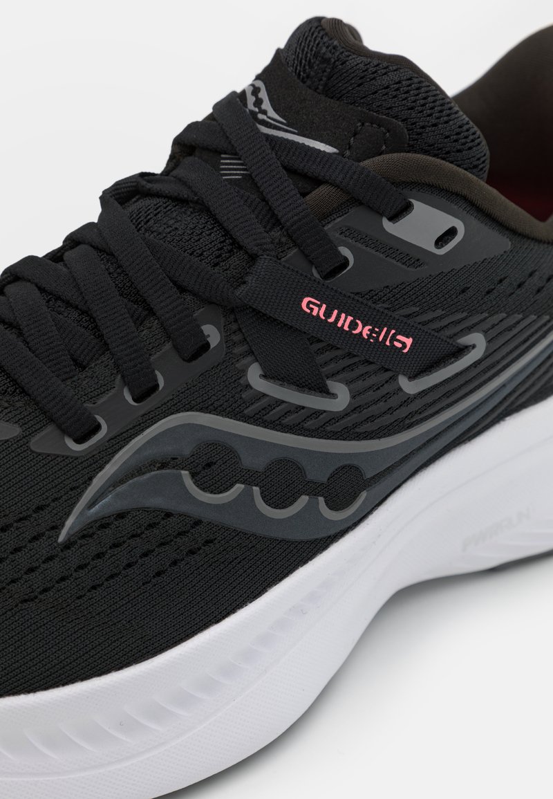 Scarpe da corsa nere con parte superiore in rete, intersuola bianca e dettagli grigi. Caratteristiche includono colletto imbottito e lacci, e un logo sul lato.