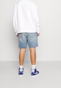 Sudadera blanca, pantalones cortos de denim azul claro y zapatillas de caña alta azules con detalles y marca blanca en la parte trasera.