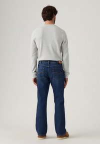 Vaqueros de denim azul con piernas rectas, cinco bolsillos y costuras en contraste. Combinados con una camiseta de manga larga gris claro.