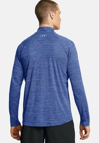 Langärmliges Athletic-Shirt in Dunkelblau mit einem strukturierten Streifenmuster. Verfügt über einen hohen Kragen und das Under Armour-Logo am Ausschnitt.