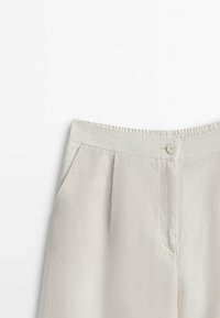 Pantalons en lin beige clair avec une fermeture à bouton, une taille élastique, des plis sur le devant et des poches latérales. Texture lisse et design ajusté.