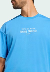 Blaues Baumwoll-T-Shirt mit kurzen Ärmeln, das mit "ADIDAS TRAINING est. 1949" in Weiß bestickt ist. Glatte Textur, Rundhalsausschnitt.