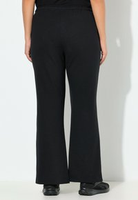 Czarne spodnie szerokie z szeroką gumką w pasie, wykonane z miękkiego, lekkiego materiału o gładkiej fakturze, bez widocznych wzorów.