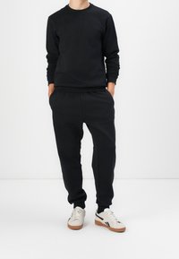 Felpa nera con maniche lunghe e collo a girocollo, abbinata a joggers neri coordinati con vita elastica. Sneakers bianche con dettagli.