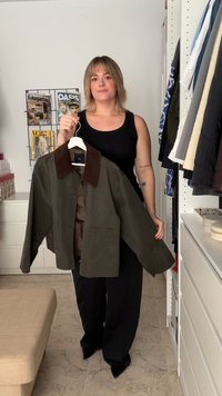 Giacca verde oliva con colletto marrone scuro, caratterizzata da una vestibilità morbida e due tasche frontali, indossata da una persona in un ambiente minimalista.