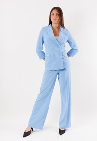 Blazer azzurro chiaro doppiopetto con ampi risvolti e maniche a tre quarti, abbinato a pantaloni a gamba larga coordinati. Tacchi a stiletto neri.