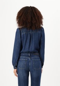 Denim antrekk som inneholder en blå, knappet skjorte med lange ermer og tilpasset midje, parret med høy midje jeans med to baklommer.
