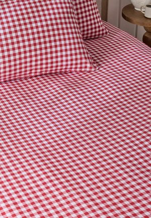 Rot-weiß kariertes Bettlaken und passende Kissenbezüge auf einem Bett mit einem Holz-Beistelltisch, auf dem eine Tasse und eine Vase stehen.
