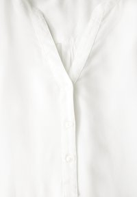 Witte blouse met een V-halslijn, voorzien van een knopenlijst en subtiele textuur, gemaakt van lichtgewicht stof.