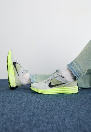 Gray running shoes with a textured upper, black logo, and bright yellow-green sole, featuring layered design and reflective accents.