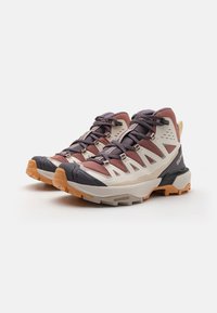 Trailrunning-Schuhe mit einem hellgrauen und maroonen Mesh-Obermaterial, dunklen grauen Akzenten und einer dicken Gummisohle mit orangefarbigen Traktionsstollen.