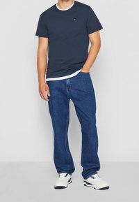 Navy blue short-sleeve T-shirt layered over a white crew neck, paired with loose-fitting blue jeans and white sneakers with navy accents.