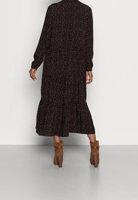 Černé šaty s dlouhými rukávy, rozptýlený oranžový květinový vzor, vrstvený lem a volný střih, doplněné o hnědé kotníkové kozačky na podpatku.