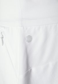 Bílý oděv s malým šedým logem v podobě glóbu a skrytým zipovým kapsou na levé straně, ukazující texturu látky a švy.