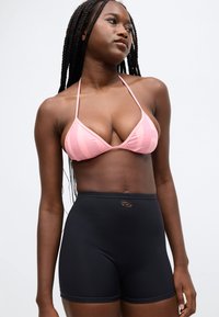 Ružový pruhovaný horný diel bikín s tenkými ramienkami v kombinácii s čiernymi plavkovými šortkami s vysokým pásom a malým logom na opasku.