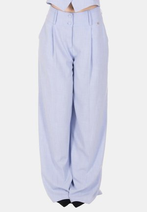 Pantaloni azzurri chiaro a vita alta, gamba larga, con pieghe frontali e chiusura con doppio bottone, indossati con scarpe nere appuntite.