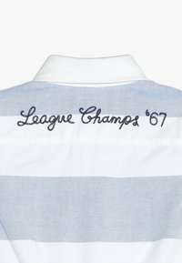 Bílo-modrá pruhovaná košile se vyšitým textem "League Champs '67" na zadním límci, s klasickým zapínáním na knoflíky.